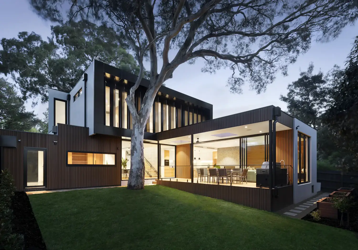 A glass and timber house at dusk, warm light spilling onto the terrace