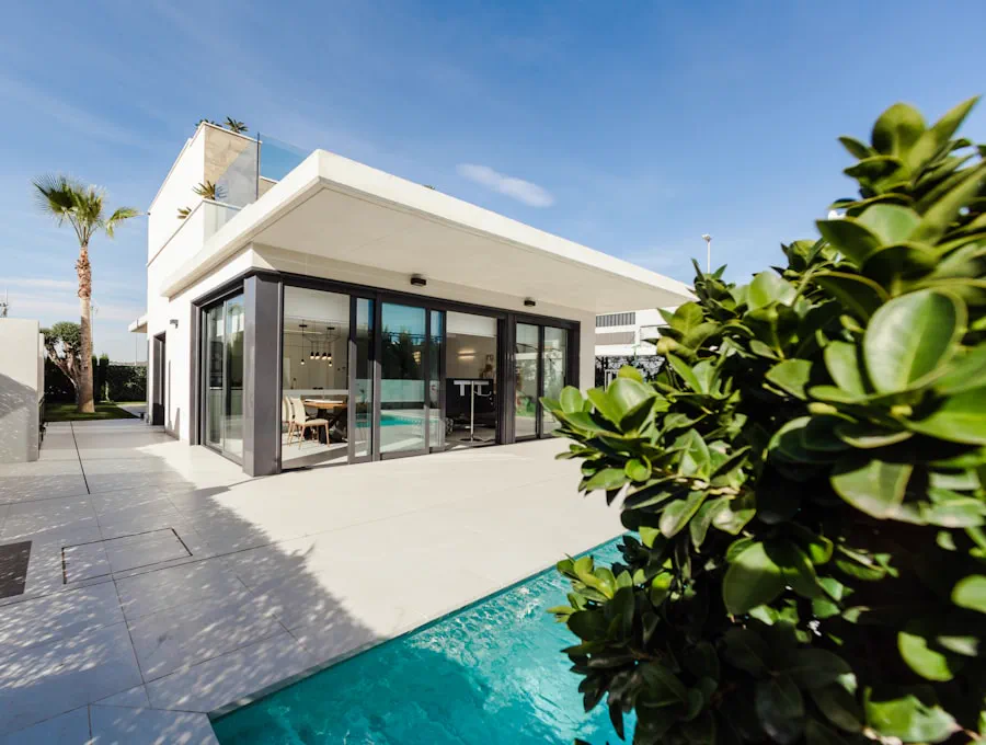 Low glass house behind clipped hedges and a palm