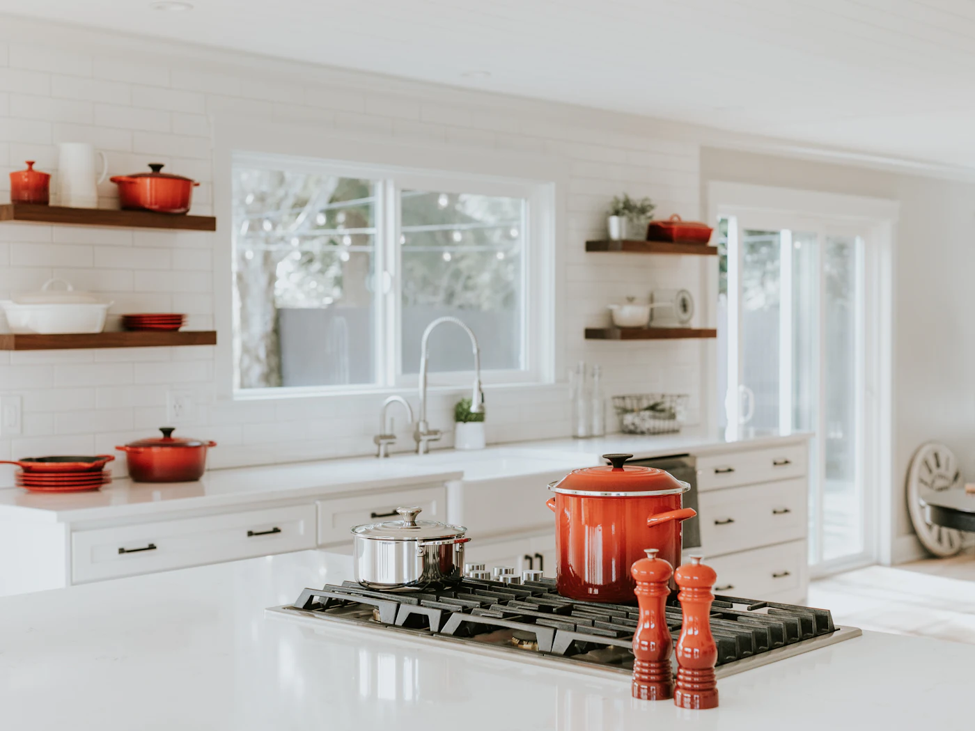 Narrow white kitchen with red cookware on open shelves